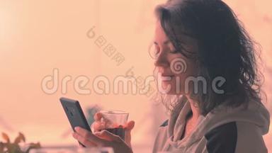 漂亮的女人在咖啡馆里用手机端着一杯热饮短信